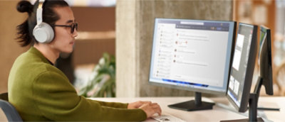 Una persona che indossa cuffie e occhiali mentre digita su una tastiera e guarda i messaggi della chat su monitor doppi in un ufficio.