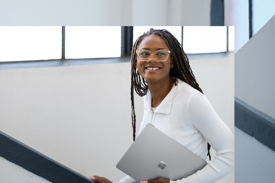 En leende kvinna som håller i en platinafärgad Surface Laptop 5 ser sig över axeln.
