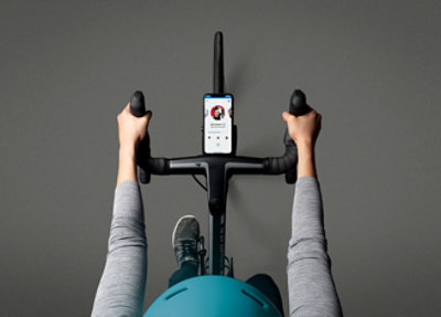 Top-down view of a person on a stationary bike holding the handlebars and looking at a smartphone mounted on the bike