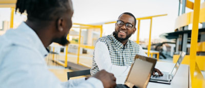 A man in glasses and a plaid shirt talking to another man.
