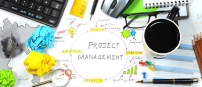 A cluttered workspace with project management flowchart, crumpled paper, glasses, ruler, pen, mouse, keyboard