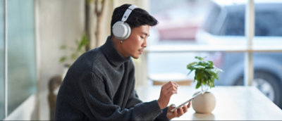 Person wearing headphones using a smartphone at a table with a small potted plant.