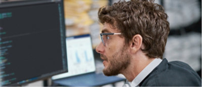 Person sitting in front of a computer monitor displaying code, in an office environment.