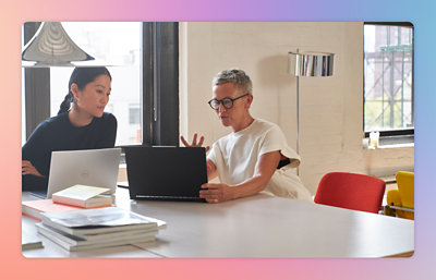 Twee personen werken op een laptop aan een tafel met boeken naast zich in een helder verlichte kamer.