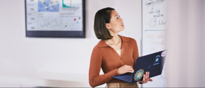 Una mujer sostiene un portátil mientras mira una pizarra con notas.
