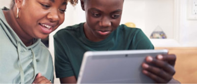 Two individuals sitting together with one holding a tablet, with their faces obscured by blurring.
