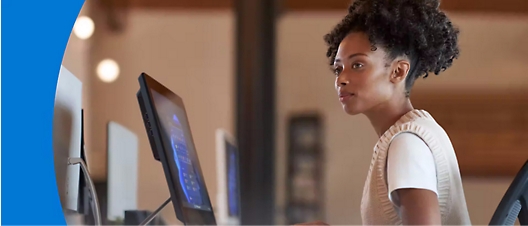 A person with curly hair sits at a computer workstation, focusing on the screen in a modern office setting.