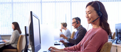 A woman wearing a headset and smiling while working on a computer.