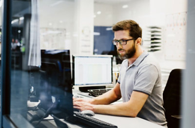 책상 앞에서 데스크톱 모니터에 연결된 노트북으로 타자를 치고 있는 사람