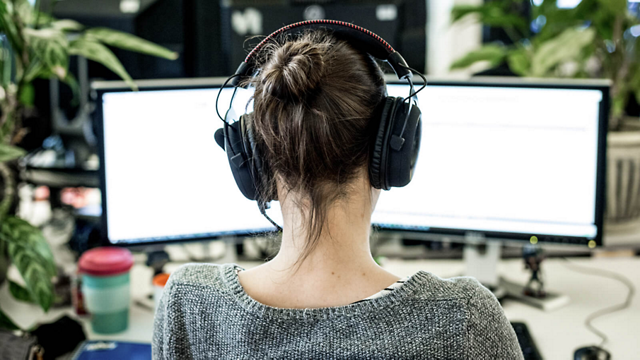 Uma pessoa com fones de ouvido trabalhando em um laptop em sua mesa.