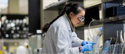 A person wearing a white lab coat and gloves