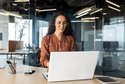 Seorang wanita duduk di depan meja menggunakan laptop.