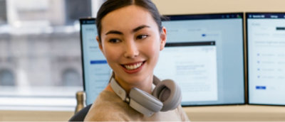 Una mujer con auriculares delante de dos monitores.