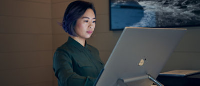 Жінка в зеленій сорочці посміхається й дивиться на екран комп’ютера.