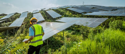Uomo con giubbotto giallo e casco in piedi davanti a pannelli solari.