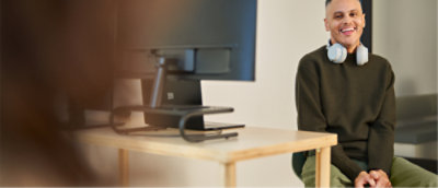 컴퓨터와 헤드폰을 목에 걸고 책상에 앉아 있는 남자