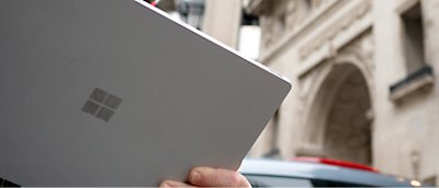 A person is holding up a surface tablet in front of a building.