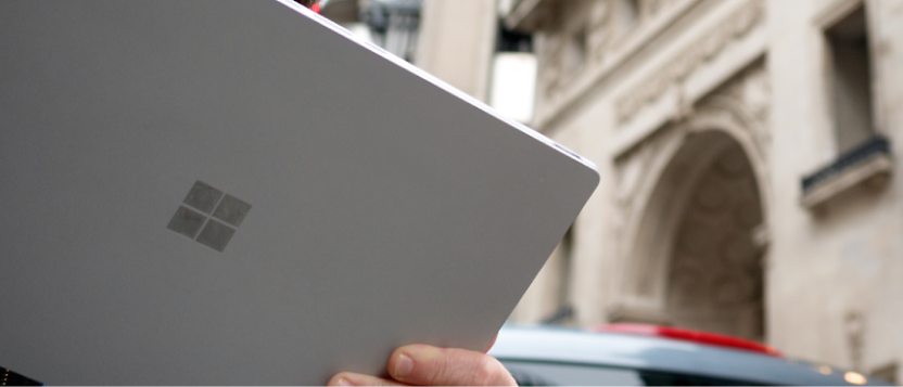 A person is holding up a surface tablet in front of a building.
