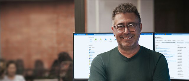 Uśmiechająca się osoba w okularach z ekranem komputera stacjonarnego w tle.