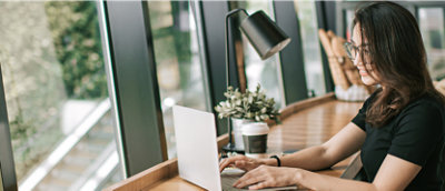 Una mujer con gafas y una camiseta negra, sentada en una mesa y usando un teléfono.