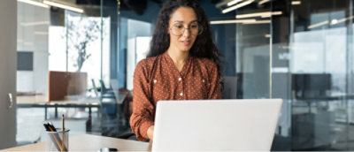A person in a polka dot shirt working on a laptop in a modern office environment.