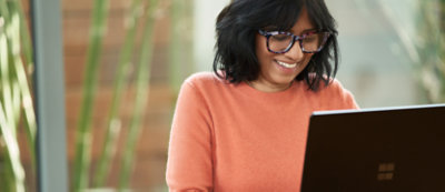 A woman wearing glasses is smiling while using a laptop.
