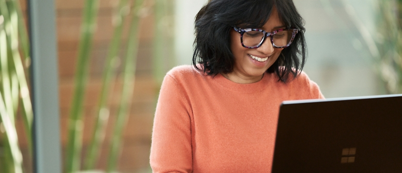 A woman wearing glasses is smiling while using a laptop.