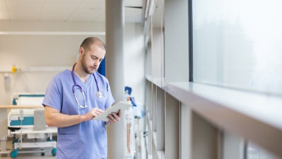 Un profesional médico de pie al lado de una ventana consultando una tableta
