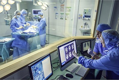 Three medical professionals performing surgery and others viewing x-rays in the room next door 