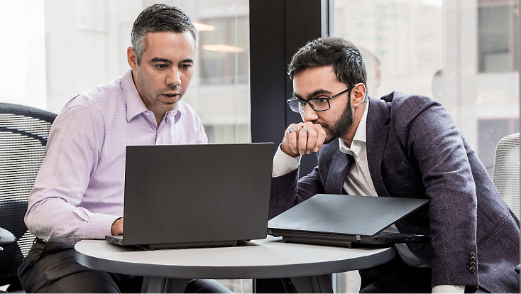 Dua orang karyawan bekerja bersama menggunakan laptop