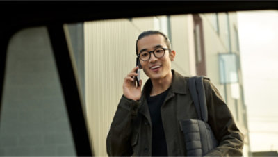 Man with glasses and a backpack smiling while talking on a smartphone outside.