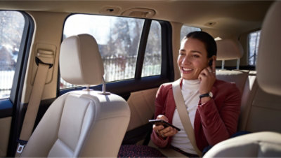 Woman sitting in the backseat of a car, holding a phone and smiling while on a call.