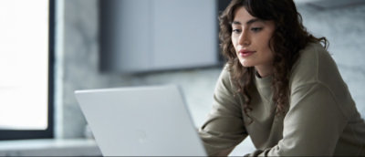Person sitting at a table working on a laptop with a window in the background.