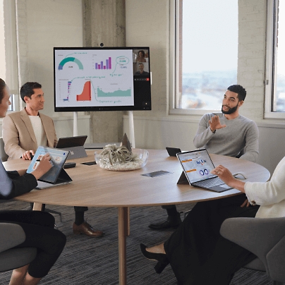 Group of people discussing while sitting around a round table with some presentation being played on big screen monitor