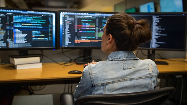 En person programmerar vid ett skrivbord och arbetar på tre skärmar
