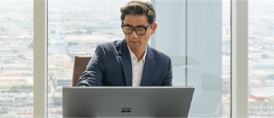 A person in a suit and glasses sitting at a desk with a computer