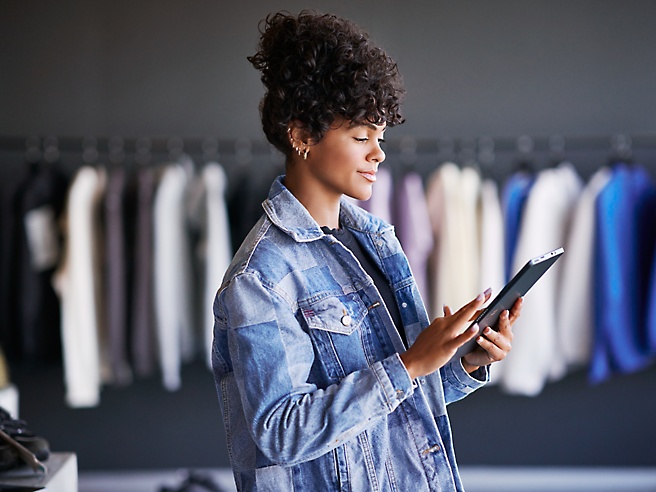 Donna con una giacca di jeans che usa un tablet in un negozio di abbigliamento