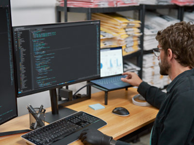 Un hombre sentado en un escritorio con dos monitores delante de él