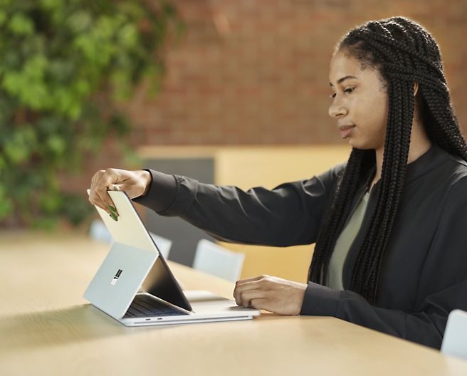Женщина держит в руках устройство Microsoft Surface Pro, сидя на стуле