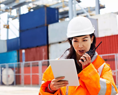 A ground staff wearing safety jacket holding tablet and talking using walkie talkie.