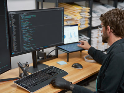 A person typing using the keyboard while the multiple monitor screens are open and placed on the table'