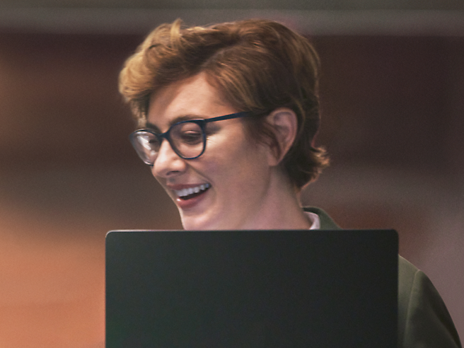 A woman wearing glasses is smiling while using a laptop