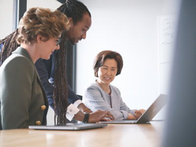 Three business people looking at a laptop in a meeting.