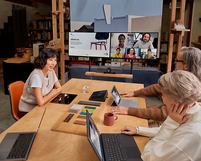 Grupo de personas en una sala de reuniones con una videollamada en una pantalla grande