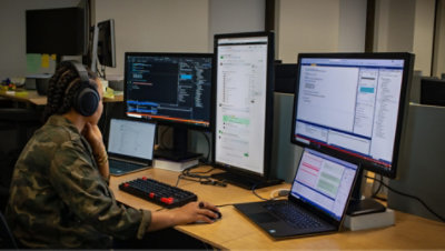 A person working at their desk with a laptop and three monitors