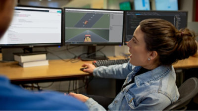 A person programming a video game and showing it to a coworker sitting next to them