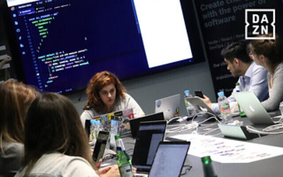 Orang-orang bekerja di ruang rapat dengan layar besar menampilkan kode