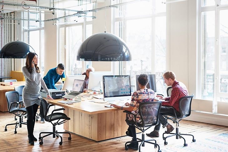 Vijf mensen die aan hun bureaus in een kantoor werken