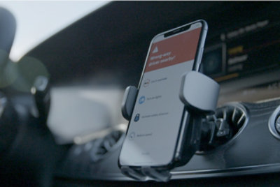 Мобильный телефон, установленный в автомобиле и отображающий оповещение о “водитель поблизости едет не по той полосе?” 