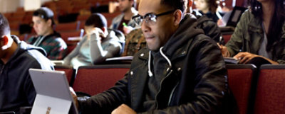 En person, der sidder i et forelæsningsauditorium og bruger en tablet